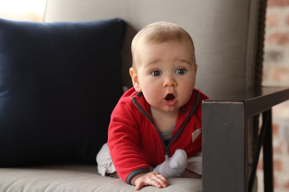 bebê de roupa vermelha sentado no sofá com cara de assustado