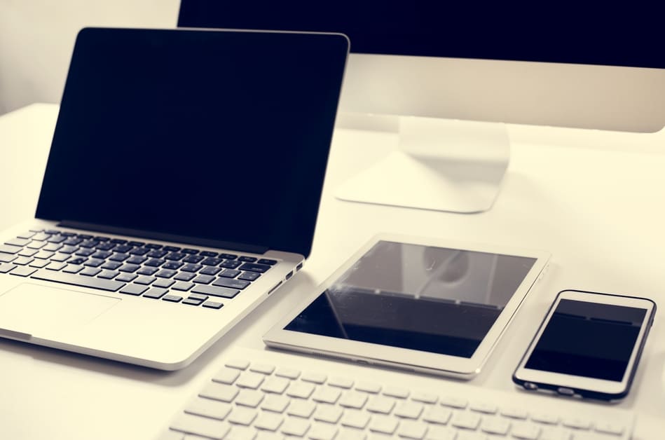 Notebook, tablet, celular, e teclado em cima de mesa