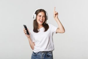 menina de cabelo solto camisa branca fone de ouvido e celular