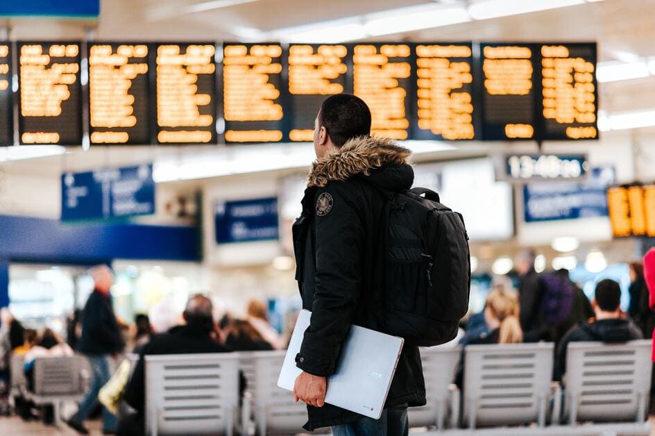 homem de costas olhando para painel de voos em aeroporto