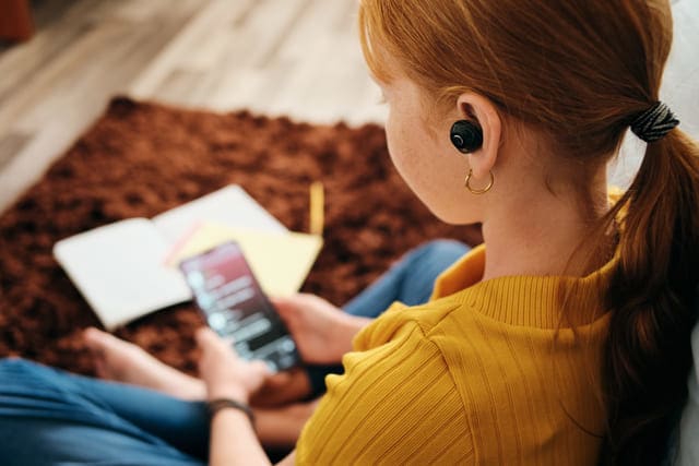menina ruiva sentada no tapete com fones ouvindo podcast
