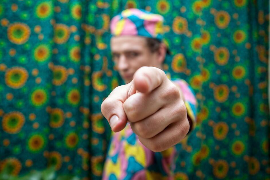 homem com camise e chapéu coloridos apontando para a câmera 