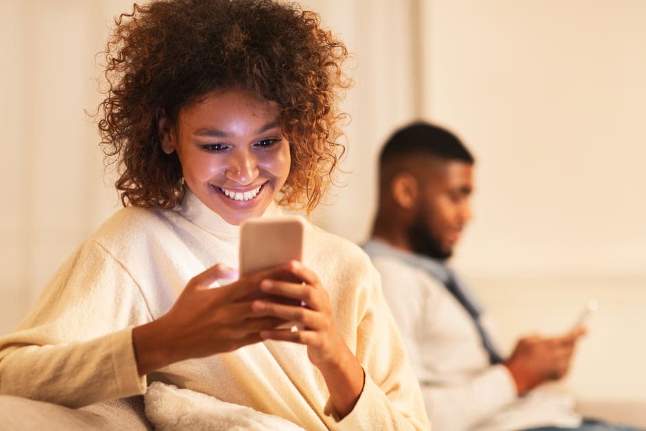 garota infiel sorrindo para o celular ao lado de namorado