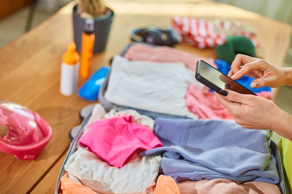 organizando mala de viagem com celular na mão 