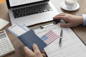 mesa com passaporte, bandeira dos estados unidos, papel, caneta, notebook, café e uma mão