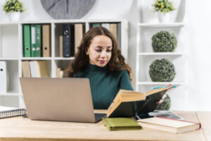 menina com laptop e livro em frente a uma estante de livros