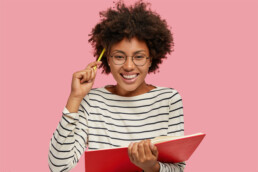 mulher sorrindo com caneta na cabeça e caderno na mao