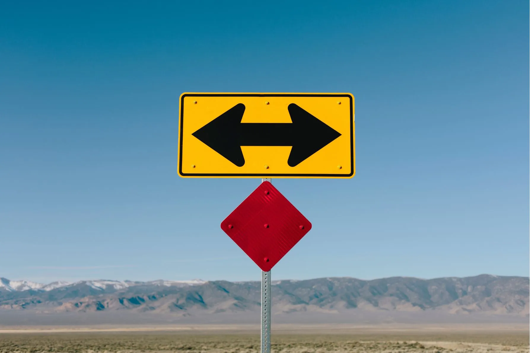 Placa de transito com duas setas apontando para sentidos opostos